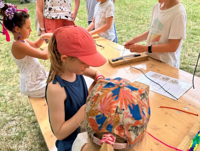Kinderen maken knutselwerkjes met touw aan een grote houten tafel tijdens een buitenactiviteit.