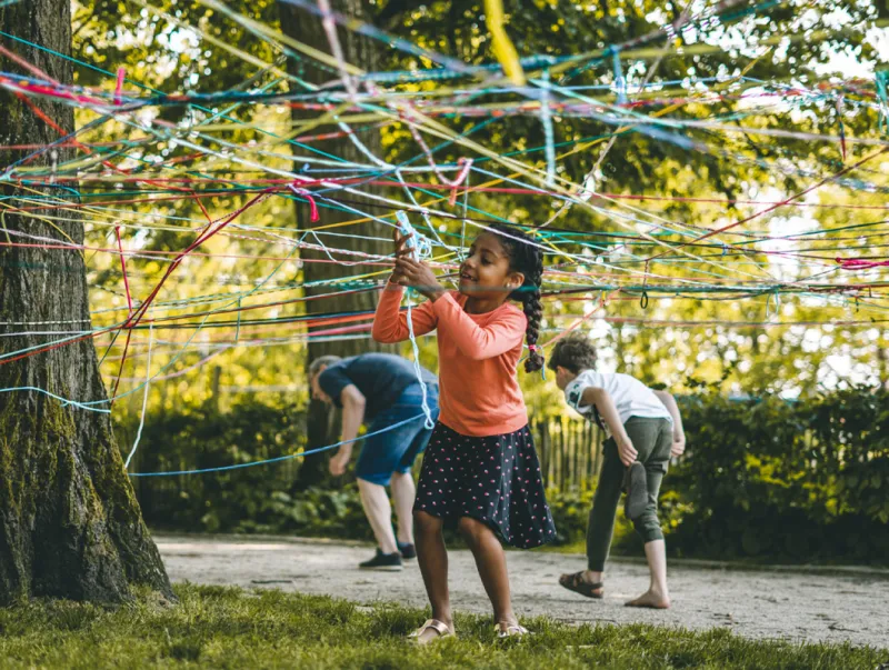 Kinderen spelen tussen kleurrijke draden die tussen bomen zijn gespannen tijdens een activiteit in het bos.